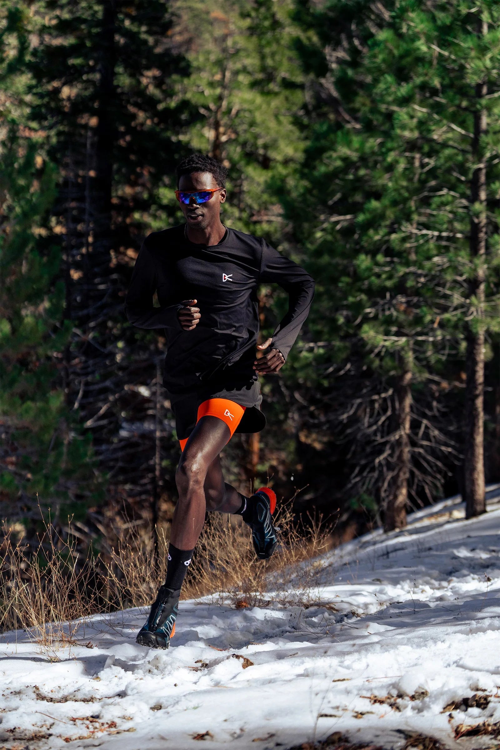 Person running on a snowy trail with trees in the background with district vision eyewear.